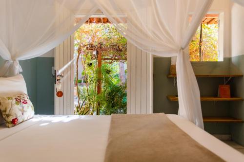 a bedroom with a bed with white curtains and a window at Vila Charme in Jericoacoara