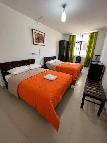 a bedroom with three beds with orange sheets and a piano at HOTEL PUNTA PARIÑAS-TALARA-PERU in Talara
