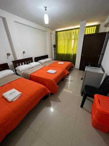 three beds in a room with orange sheets at HOTEL PUNTA PARIÑAS-TALARA-PERU in Talara