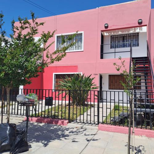 Um edifício cor-de-rosa com uma vedação à frente. em Temporarios Alto Verde em Córdoba