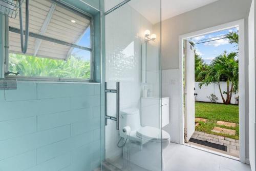 a white bathroom with a toilet and a glass door at Wilton Manors Oasis with an outdoor Pool in Fort Lauderdale