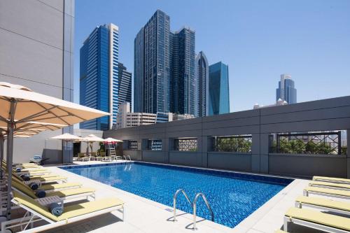 a swimming pool with lounge chairs and a city skyline at Rove Trade Centre in Dubai