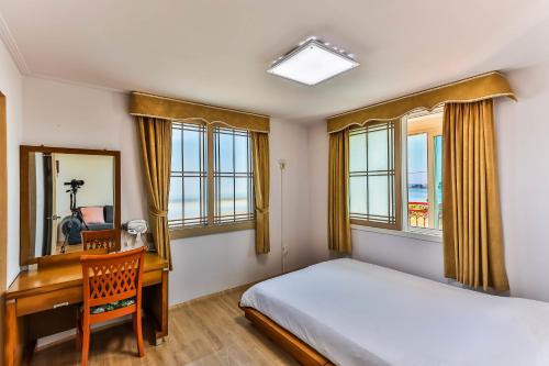 a bedroom with a bed and a desk and windows at Sea Eco Beach in Jeju