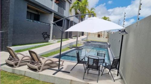 einen Tisch mit Stühlen und einen Sonnenschirm neben einem Pool in der Unterkunft Cobertura Vista Mar Carapibus - Cariri Praia - Apartamento completo com 02 quartos in Conde
