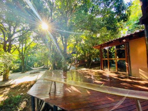 una terraza de madera con el sol brillando entre los árboles en Kalis Inn en Alto Paraíso de Goiás
