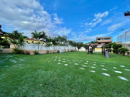 a large grassy yard with a fence and palm trees at Casa Em condomínio portaria24 horas,piscina in Cabo Frio