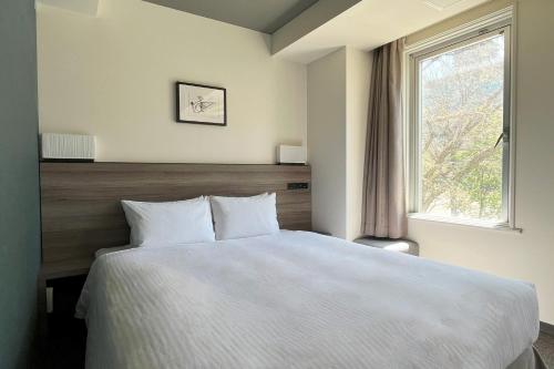 1 dormitorio con cama blanca y ventana en Best Western Sapporo Odori Koen, en Sapporo