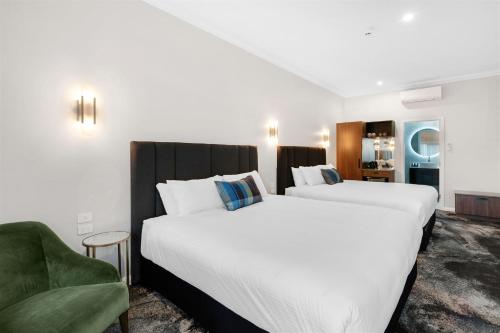 two beds in a hotel room with a green chair at St Hugh Hotel Wagga Wagga in Wagga Wagga