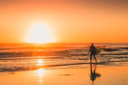 a man walking on the beach with a surfboard at Villa Shakti Canggu in Canggu