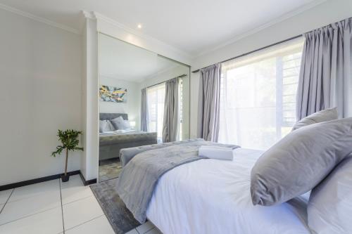 - une chambre avec un lit blanc et une grande fenêtre dans l'établissement Luxury Home with an Office & Backup Power, à Sandton