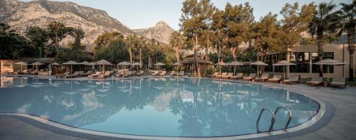 a large swimming pool with chairs and mountains in the background at Balmy Beach Resort Kemer in Kemer
