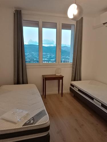 une chambre avec deux lits, une table et des fenêtres dans l'établissement Appartement Lumineux Vue Panoramique, à Ajaccio
