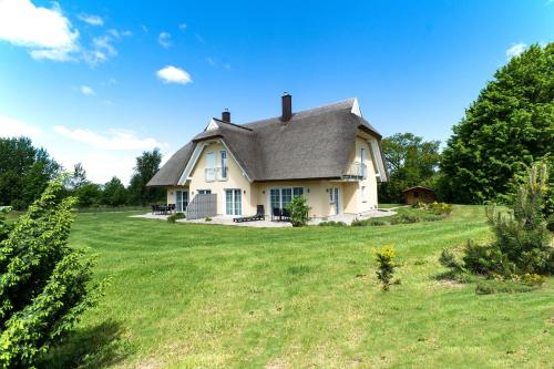 a white house with a gray roof on a green field at Strandvilla "Babette" - BALO B, direkt am Meer, mit Sauna in Lobbe