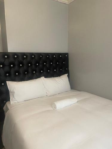 Cama blanca con cabecero negro y almohadas blancas en Stay Inn Lodge Boksburg, en Boksburg