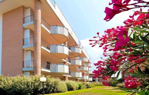 un edificio con flores rosas delante de él en ISA-Apartments for 4 people, 2 bedrooms, in Residence with swimming pool in San Vincenzo, just 600 meters from the sea, en San Vincenzo