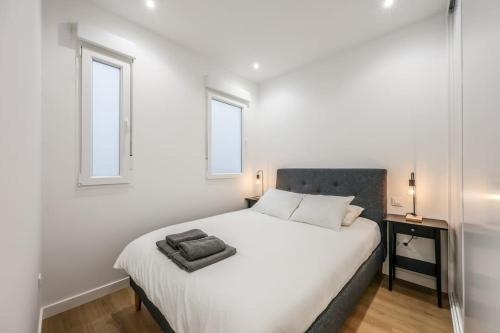 a white bedroom with a bed and two windows at MyHouseSpain - Glamour y confort cerca del Retiro in Madrid