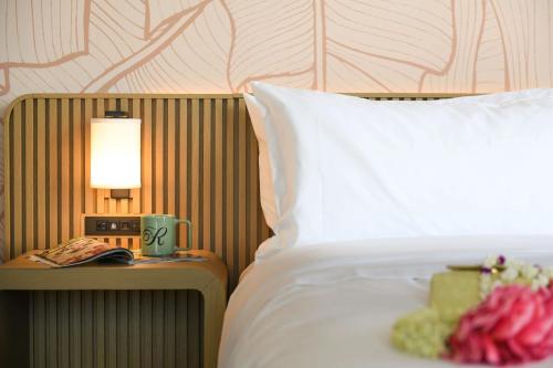 a bed with a white pillow and a table with a lamp at The Ambassador of Waikiki, Tapestry Collection by Hilton in Honolulu