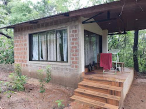 a small brick house with a porch and a chair at Vanoshi Forest Homestay,Kudase in Maneri