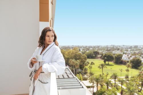a woman in a white robe holding a cup of coffee on a balcony at Sofitel Rabat Jardin Des Roses in Rabat