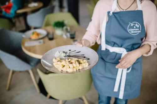 a woman in a blue apron holding a plate of food at Camping Passeier Glamping Aurum in Saltusio