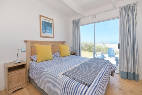 Un dormitorio con una cama con almohadas amarillas y una ventana. en Chez Nous In Arniston, en Arniston