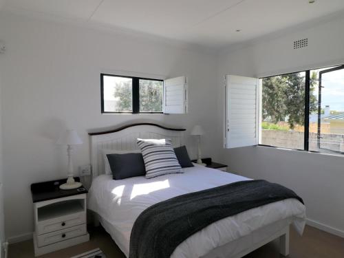 a white bedroom with a bed and two windows at Eland's Rest In Arniston in Arniston