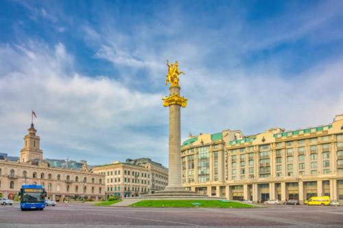 a tall monument in front of a building with a bus at Hotel Middleton in Tbilisi City