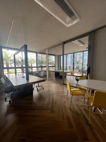 una oficina con mesas, sillas y ventanas grandes en Lar no Bueno en Goiânia