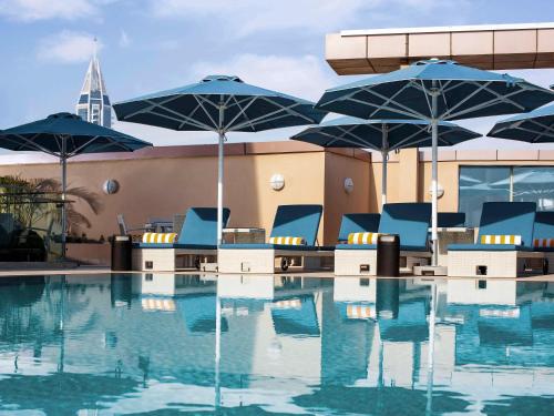a pool with blue chairs and umbrellas in a building at Pullman Dubai Jumeirah Lakes Towers in Dubai