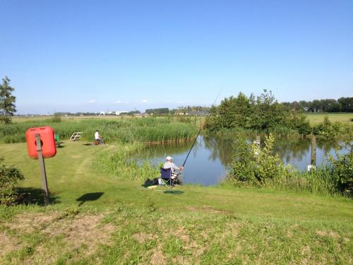 a man sitting in a chair fishing by a pond at Vakantiepark Koningshof in Rijnsburg