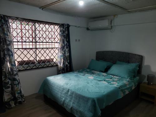 a bedroom with a bed with blue sheets and a window at Mango Vert Apartment in Arima
