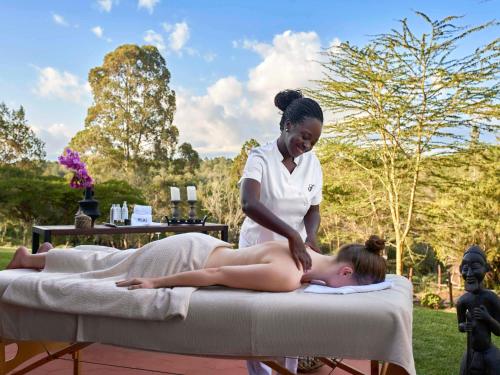 Kobieta leży na łóżku masażu z terapeutą. w obiekcie Fairmont Mount Kenya Safari Club w mieście Nanyuki