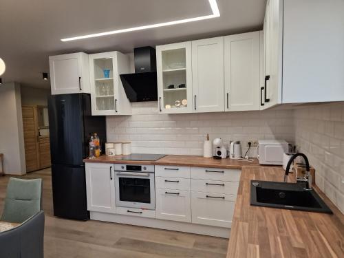 a kitchen with white cabinets and a black refrigerator at Mālu namiņš in Ķekava