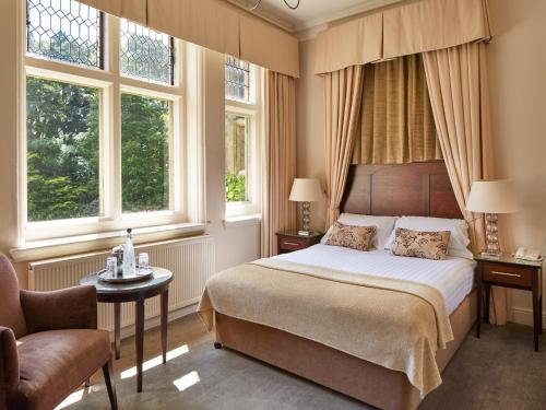 um quarto com uma cama, uma cadeira e janelas em Macdonald Frimley Hall Hotel & Spa em Camberley