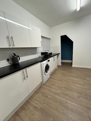 a kitchen with white cabinets and a washer and dryer at Spacious 5-Bedroom Urban Haven in Luton