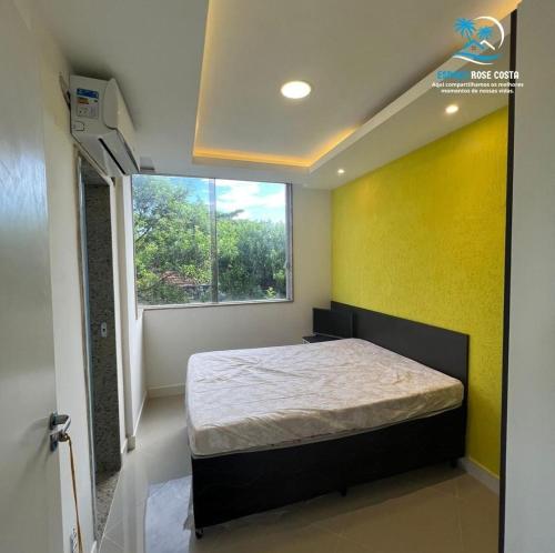 ein Schlafzimmer mit einem Bett mit gelber Wand und einem Fenster in der Unterkunft Espaço Rose Costa in Niterói