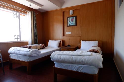 two beds in a room with wood paneling at Hotel Mon Paradise in Tawang