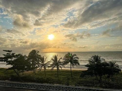 a sunset over the ocean with palm trees on the beach at Excelente Flat beira-mar in Cabedelo