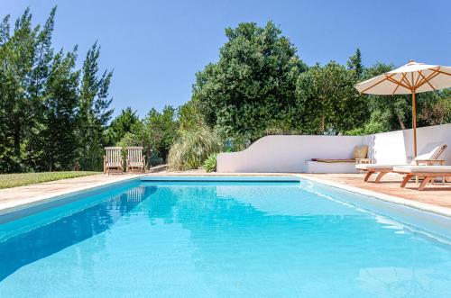 a swimming pool with an umbrella and a table and chairs at Casa Litoral in Melides