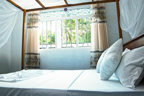 1 dormitorio con 1 cama y ventana con cortinas en The White Villa, en Hikkaduwa