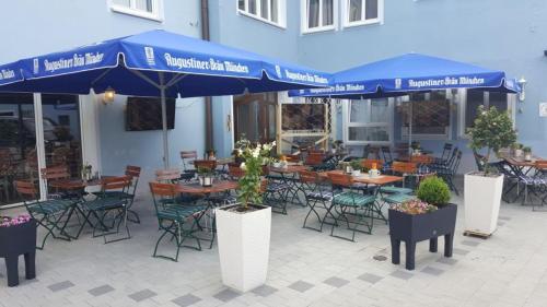 eine Terrasse mit Tischen, Stühlen und blauen Sonnenschirmen in der Unterkunft Posthotel Traube in Donauwörth