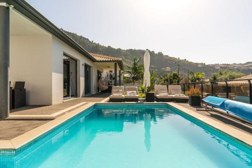 a swimming pool with chairs and a house at Casa Mia, a Dream Spot With Heated Pool in Arco da Calheta