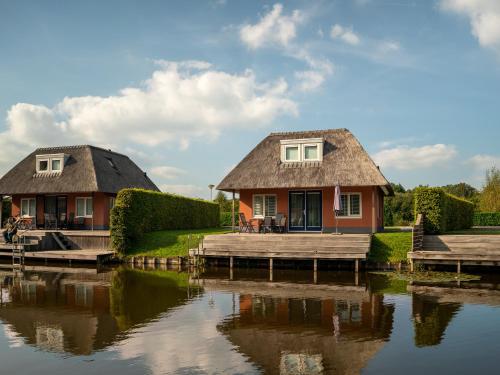 a house with a thatched roof next to a river at Summio Waterpark De Bloemert in Zuidlaren