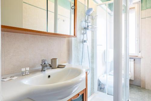 La salle de bains est pourvue d'un lavabo blanc et d'une douche. dans l'établissement Homiday- Free Parking - Design Flat - Ospedale Cisanello, à Pise