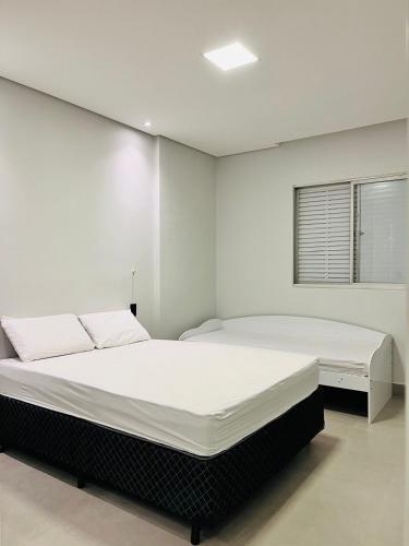 a white bedroom with a large bed and a window at Cara da Praia in Guarujá