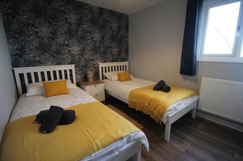 a bedroom with two beds with yellow sheets and a window at Pollan-Na Clach Cabin in Lairg