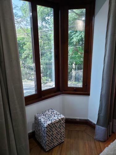 a room with two large windows and a ottoman in front at Pousada Monte Sião in Sao Paulo