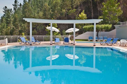 a pool with a gazebo and chairs and umbrellas at Apartamentos do Lago in Ferreira do Zêzere