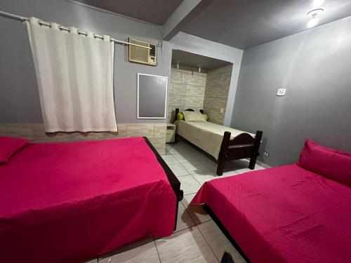 um quarto com 2 camas com lençóis cor-de-rosa e uma televisão em Casinha Vilarejo em Cabo Frio