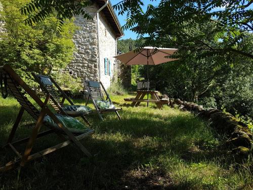 a patio with chairs and an umbrella in the grass at Gîte du Puy in Saint-Fortunat-sur-Eyrieux